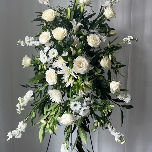 Tall white floral standing spray with roses and daisies on a black easel