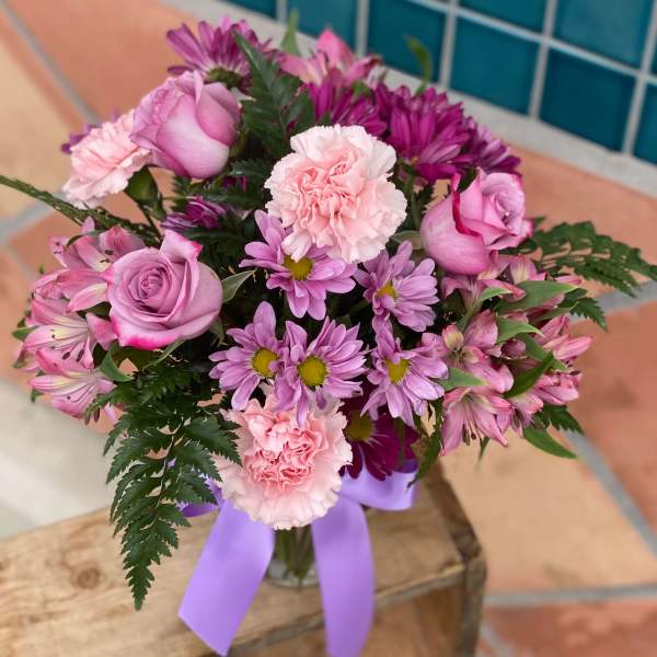 Pink and purple bouquet in a glass vase with a lavender ribbon