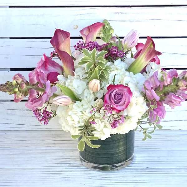 Pink and white flower arrangement with roses, calla lilies, and tulips in a glass cylinder vase.