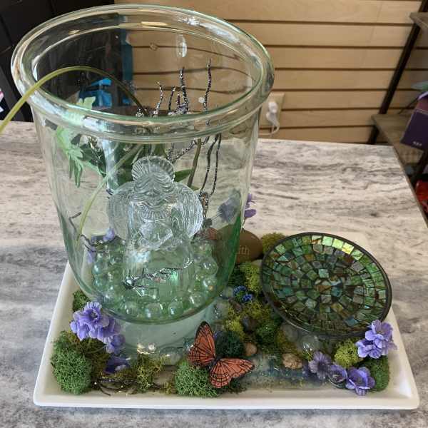 Glass fountain display with purple flowers and butterfly accents on a tray
