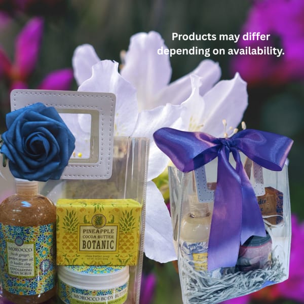 Gift set with body scrub, soap, and lotion beside white flowers and purple ribbon