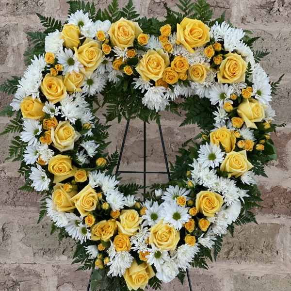 Heart-shaped floral wreath with yellow roses and white daisies on a stand