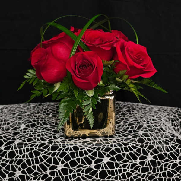 Red roses arranged in a gold square vase with green foliage