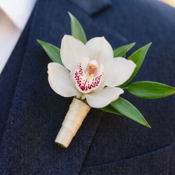White orchid boutonniere with green leaves on a dark suit lapel
