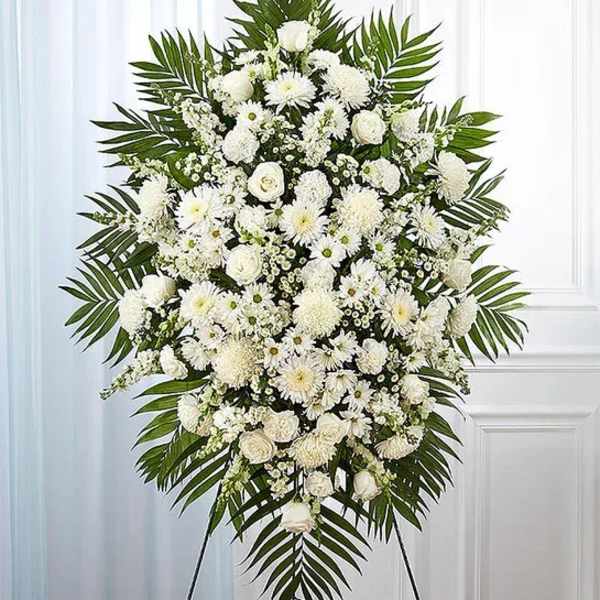 Large white funeral spray with mixed blooms and palm fronds on a stand