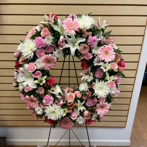 Pink and white floral wreath on a black stand with pink bows