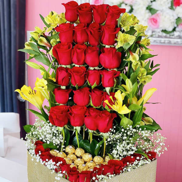 Tall box arrangement of red roses with yellow lilies and gold chocolates