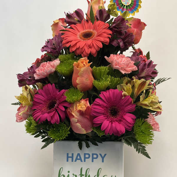 Birthday flower arrangement in a striped gift box with a "Happy Birthday" topper
