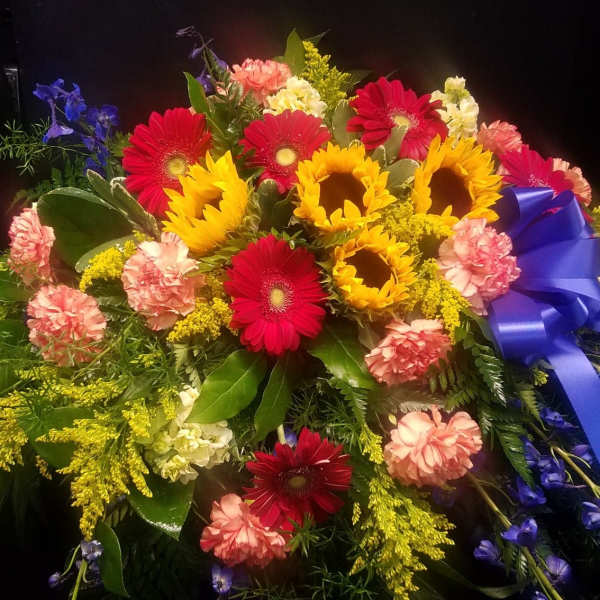 Colorful bouquet with sunflowers, red gerbera daisies, and pink carnations tied with a blue ribbon
