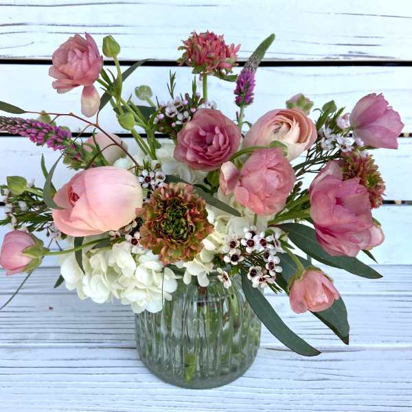 Small glass vase with pink ranunculus and mixed flowers in a loose, airy arrangement