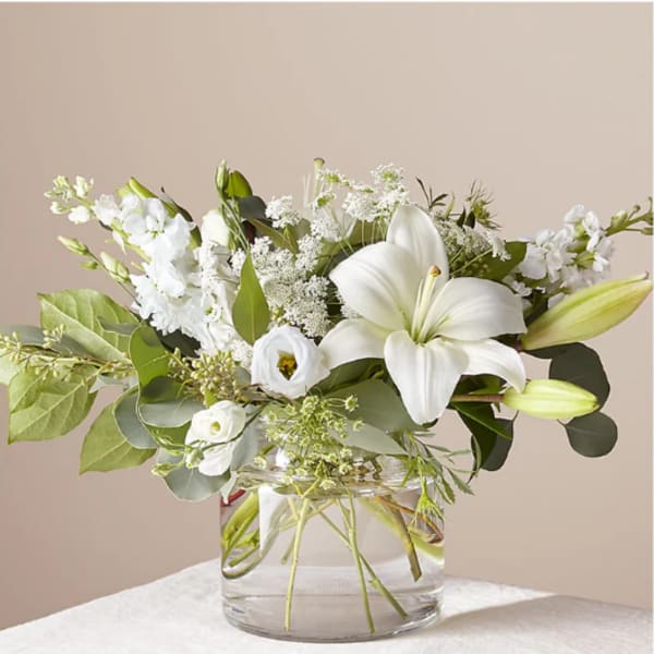 White lilies and small white flowers in a clear glass vase