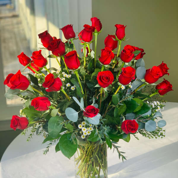 Red roses arranged in a clear glass vase with small white filler flowers