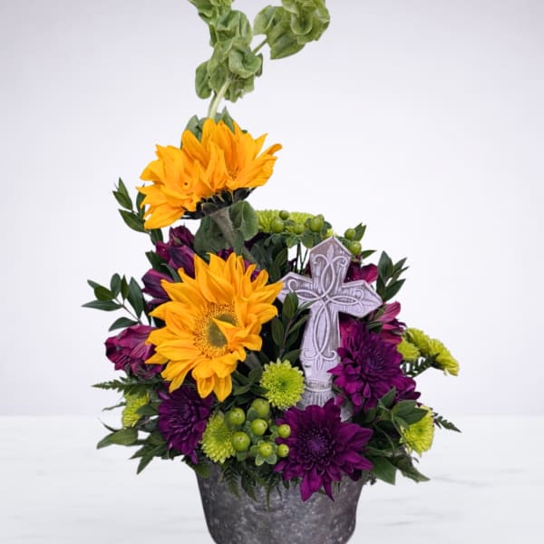 Purple and yellow floral arrangement in a metal pot with a decorative cross