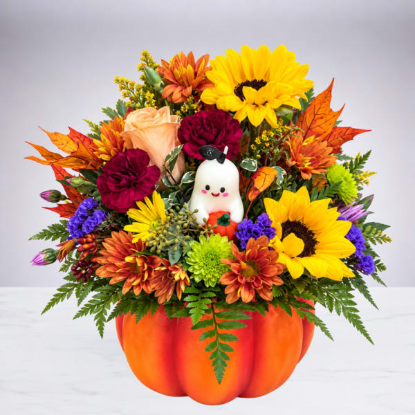 Fall flower arrangement in a pumpkin container with a small ghost decoration