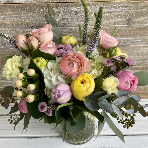 Pastel bouquet of roses, ranunculus, and hydrangeas in a clear glass vase