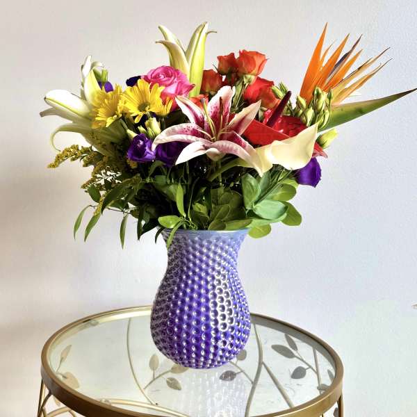 Mixed bouquet in a purple textured vase with lilies, roses, and daisies