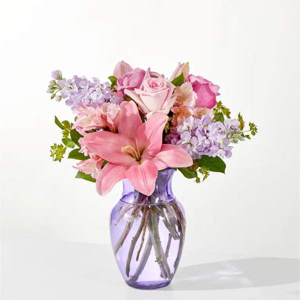 Pink lilies and roses arranged in a purple glass vase