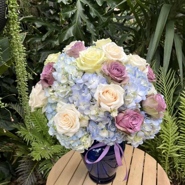 Bouquet of pastel roses and blue hydrangeas in a dark vase