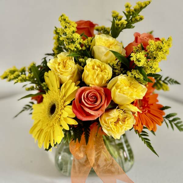 Mixed bouquet of yellow and orange flowers in a glass vase with an orange ribbon