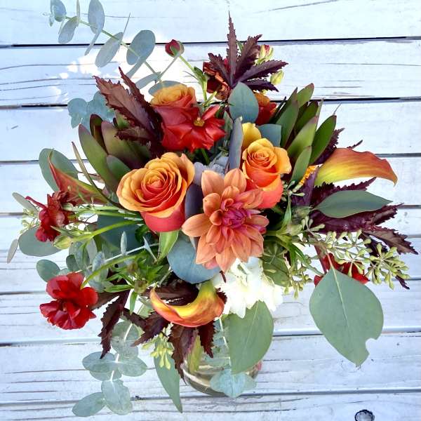 Mixed bouquet of orange roses, red blooms, and eucalyptus in a glass vase
