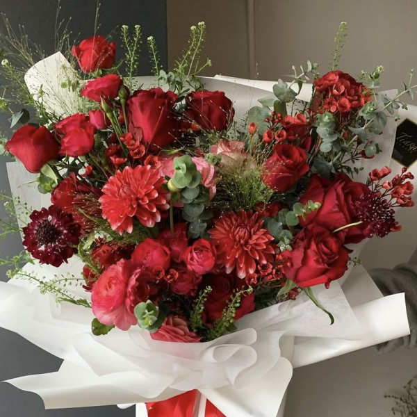Bouquet of red roses and pink blooms wrapped in white paper