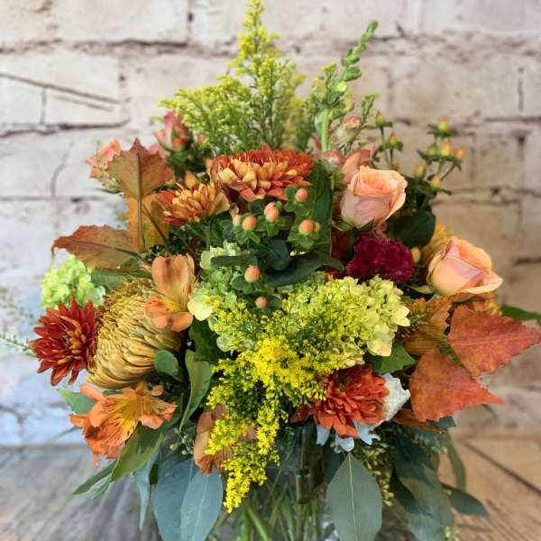 Autumn bouquet with orange and yellow flowers in a clear glass vase