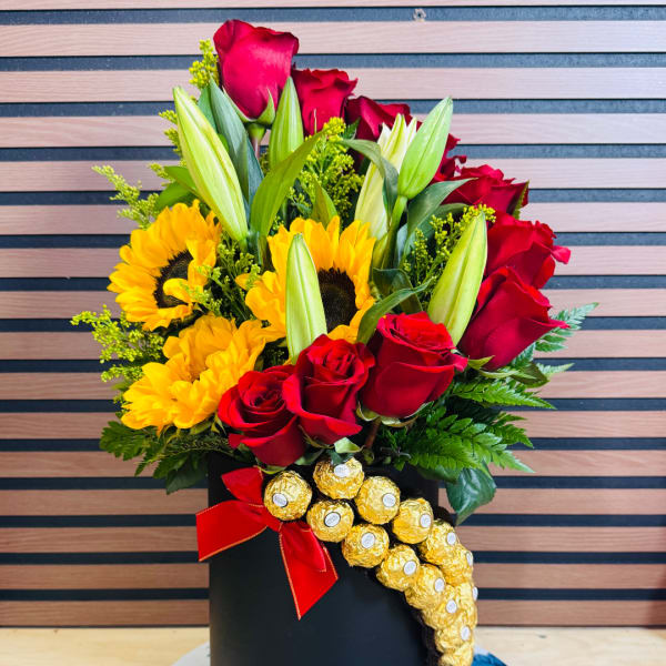 Bouquet of red roses, yellow sunflowers, and lilies in a black box with chocolates