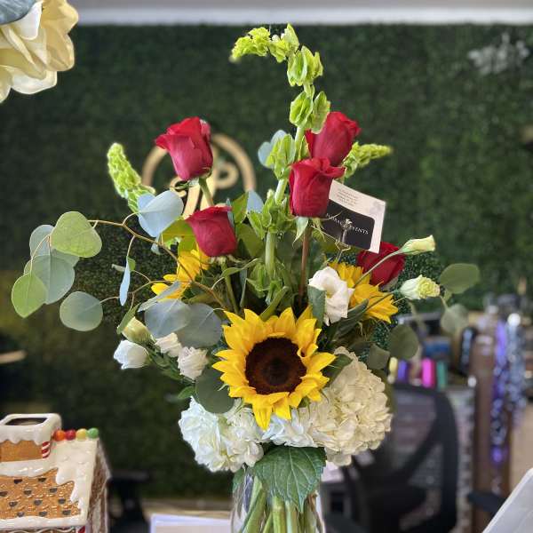 Mixed bouquet in a clear glass vase with red roses, a sunflower, and white hydrangeas.