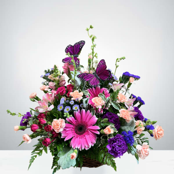 Mixed pink and purple flower arrangement in a basket with butterfly accents