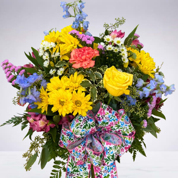 Bright mixed bouquet in a glass vase with a floral ribbon.