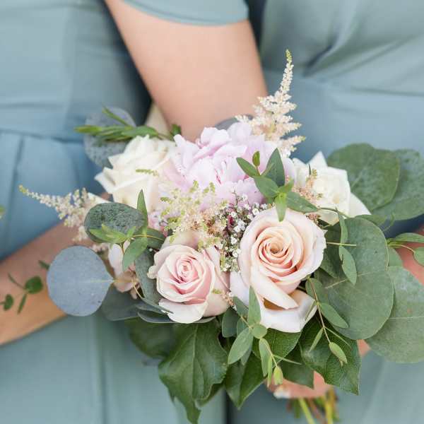 Handheld bouquet of pale pink and white roses with greenery