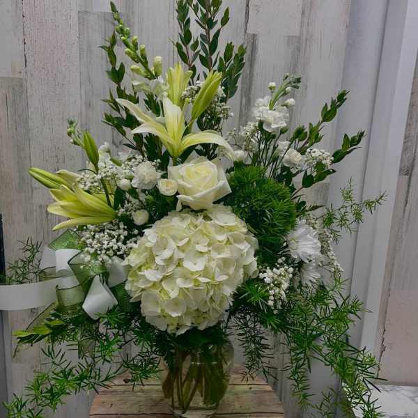 White floral arrangement with lilies, roses, and hydrangea in a glass vase