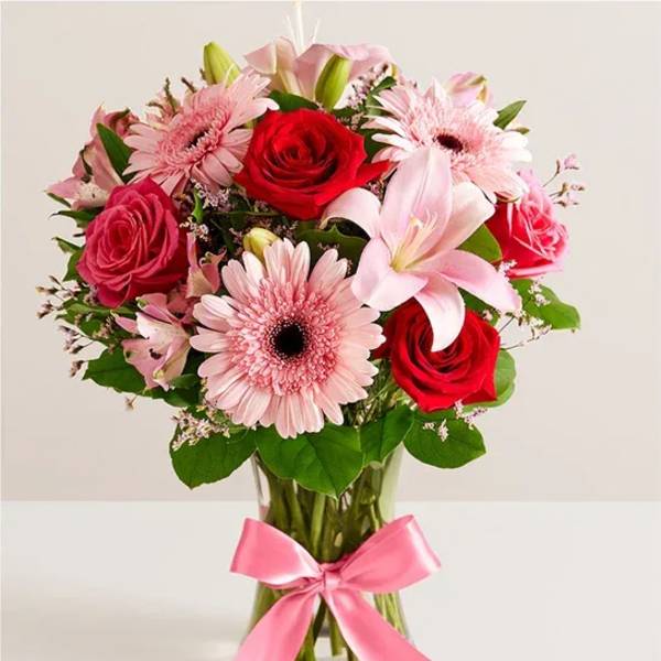 Pink and red flower bouquet in a glass vase with a pink ribbon