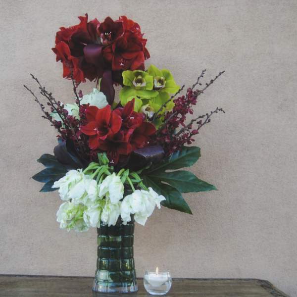 Tall floral arrangement with red, green, and white blooms in a glass vase