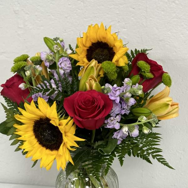 Bouquet of sunflowers, red roses, and lilies in a glass vase