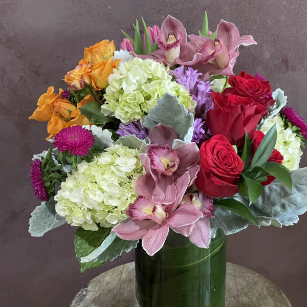 Mixed bouquet of roses, orchids, and hydrangeas in a green vase
