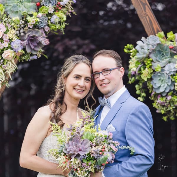Bride and groom holding a bouquet in front of a floral arch