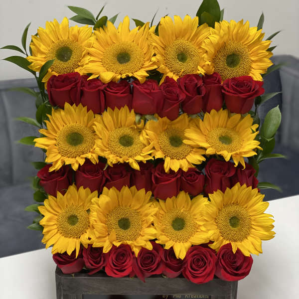 Sunflowers and red roses arranged in a wooden box with a pink ribbon
