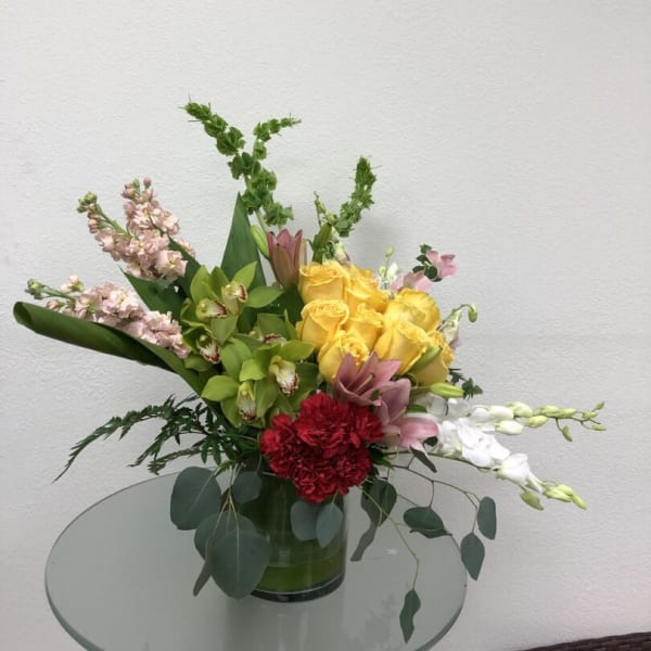 Mixed bouquet in a glass vase with yellow roses, pink blooms, and white orchids