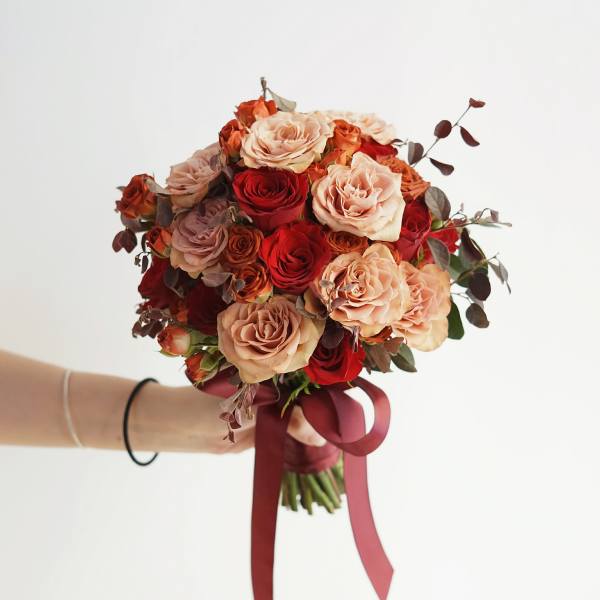 Handheld bouquet of red and blush roses tied with a burgundy ribbon