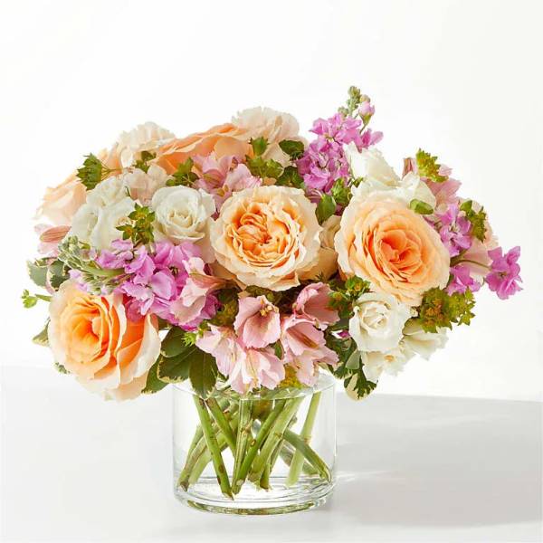 Peach and white roses with pink flowers in a clear glass vase