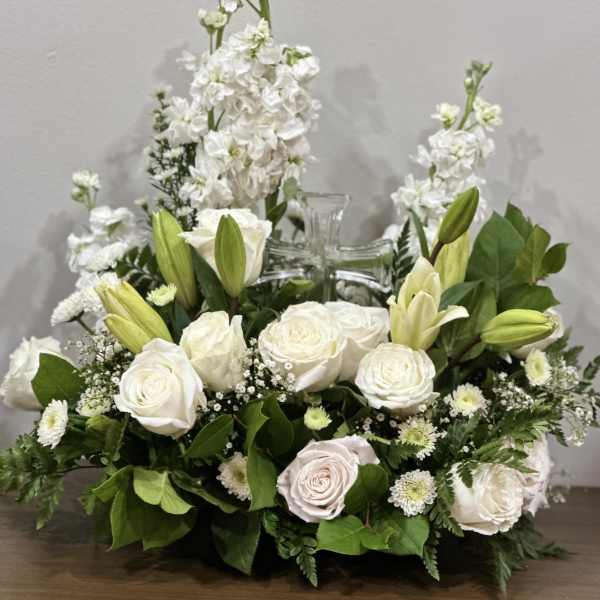 White roses and lilies arranged around a clear glass cross