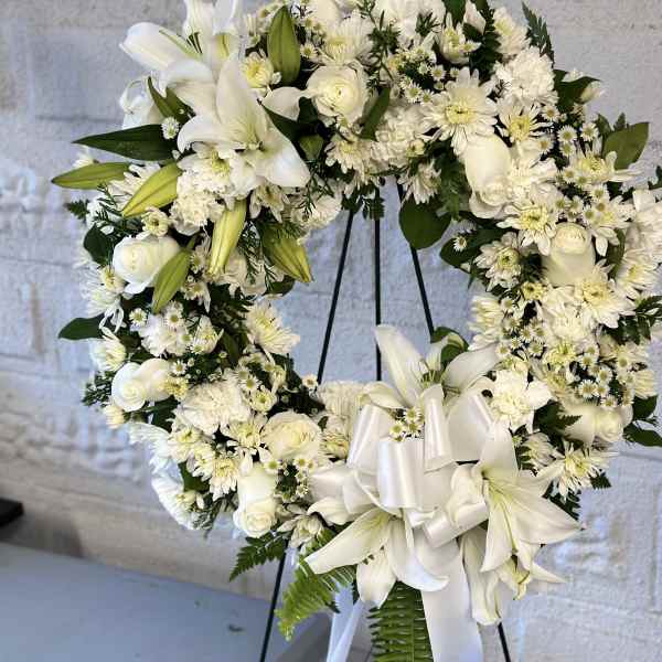 White floral wreath with lilies, roses, and daisies on a stand