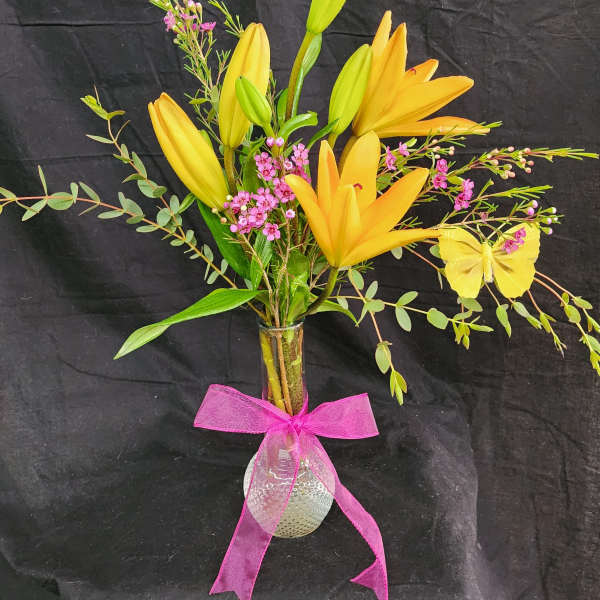 Yellow lilies in a glass vase with pink flowers and a pink ribbon