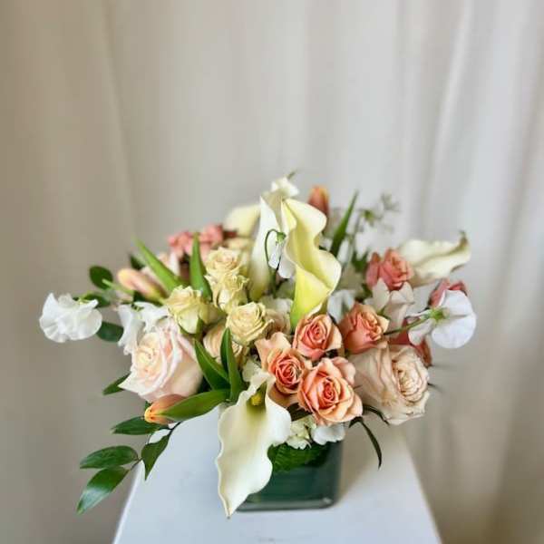 Arrangement of peach roses and white calla lilies in a square glass vase