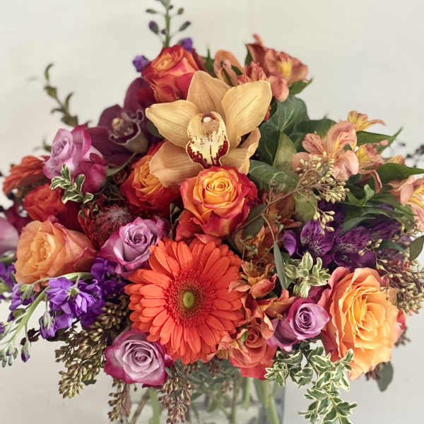 Mixed bouquet of roses, gerbera daisies, and orchids in a glass vase