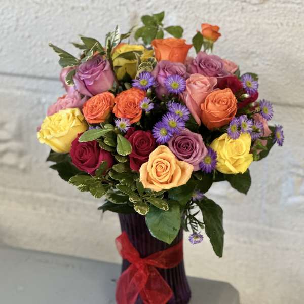 Bouquet of multicolored roses with purple daisies in a vase
