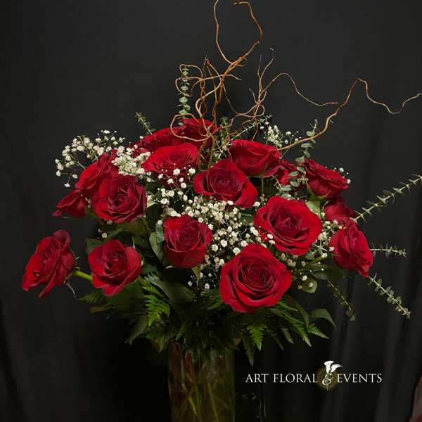 Red roses arranged in a tall glass vase with white baby's breath