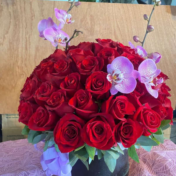 Red rose arrangement with lavender orchids in a black vase