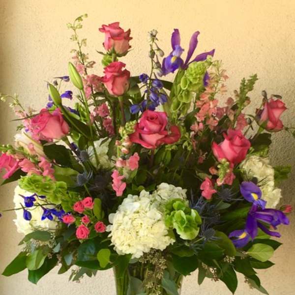 Tall mixed bouquet of pink roses, purple irises, and white hydrangeas in a glass vase